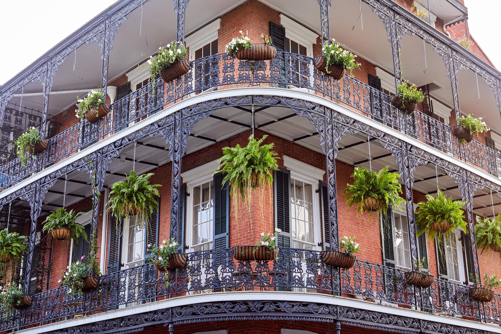 A red brick building with ornate ironwork balconies and many potted plants
