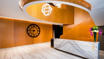 A modern lobby with a marble desk, wooden accents, a large clock, and decorative lighting.