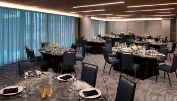 The image shows an elegantly set dining room with round tables, chairs, and tableware, likely prepared for an event or banquet.