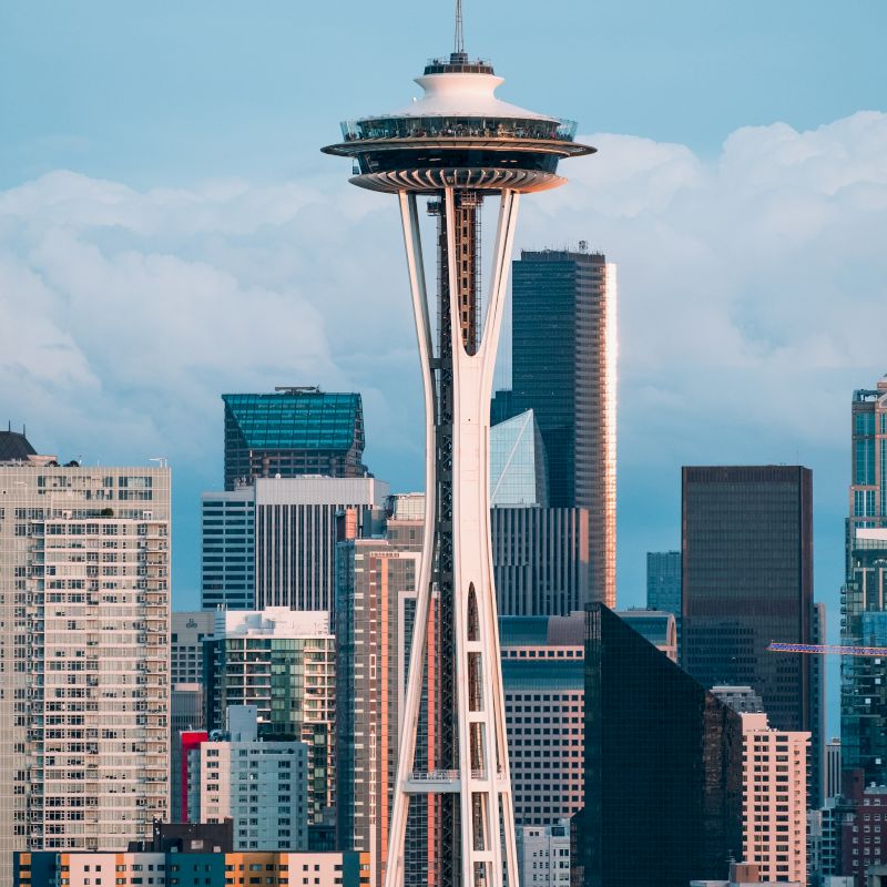 The image features the Space Needle with a backdrop of Seattle's skyline, showcasing various buildings under a partly cloudy sky.