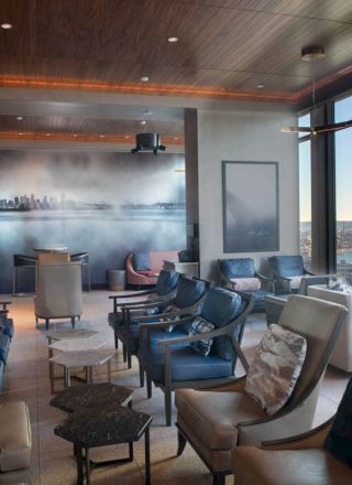A modern lounge with comfortable chairs, large windows offering a scenic view, and a mural on the wall depicting a city skyline.