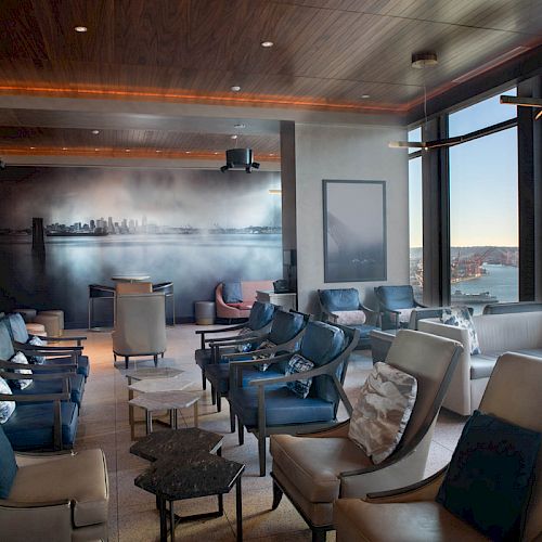 This image shows a stylish lounge with modern seating, a wall mural, and large windows offering a scenic view of the waterfront.