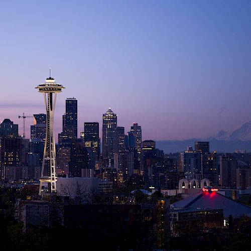 Seattle skyline at dusk features the Space Needle, city buildings, and Mount Rainier in the background.