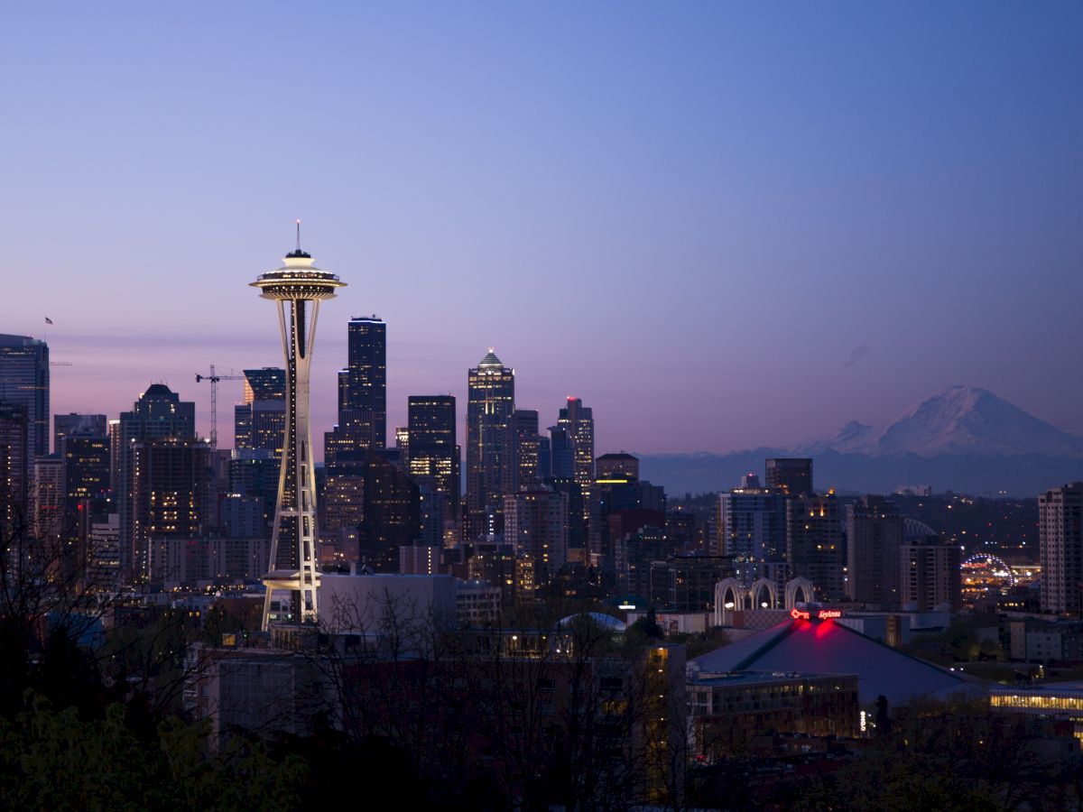 The image shows a skyline view of Seattle at dusk, featuring the Space Needle and Mount Rainier in the background.